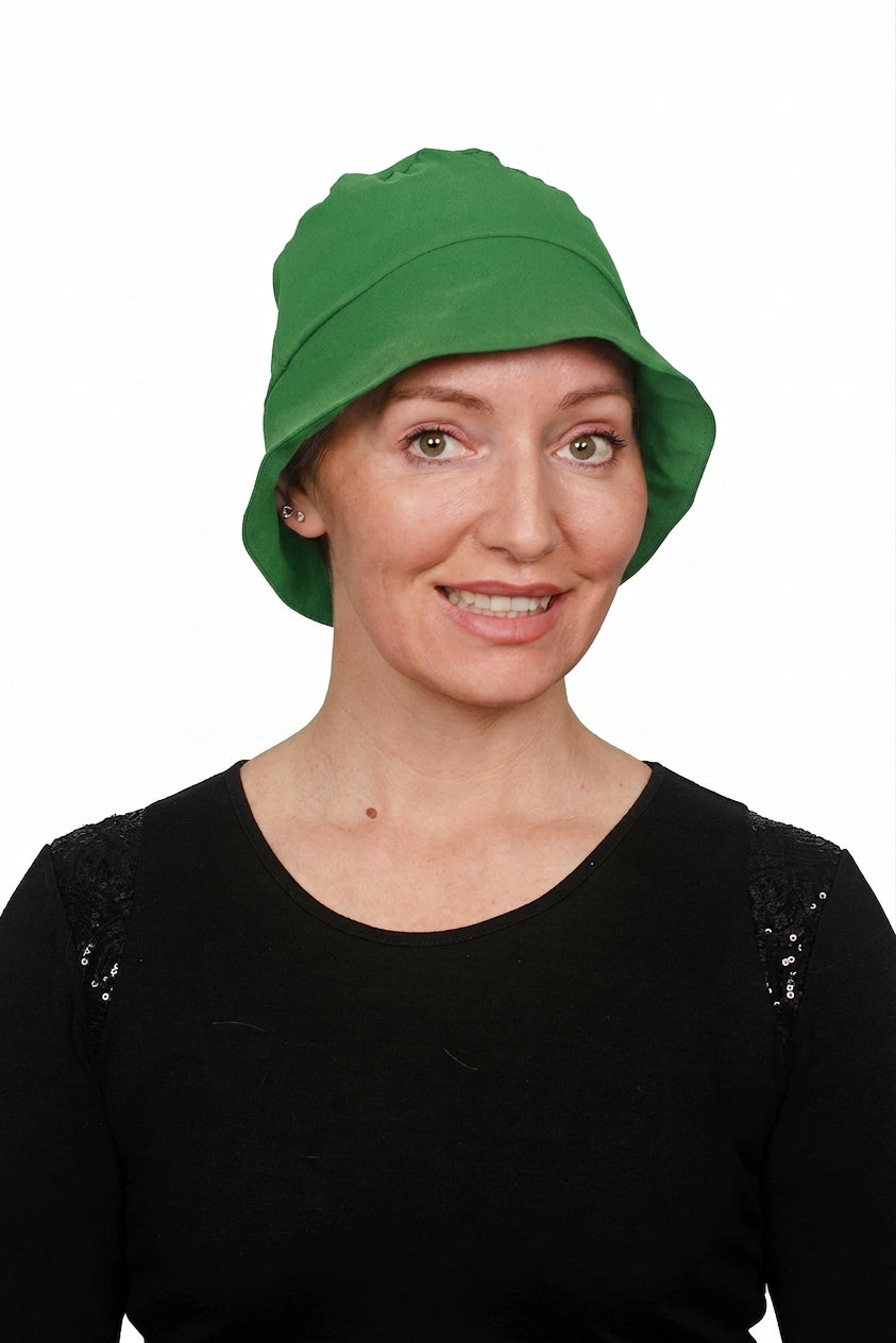A woman wearing a cancer bright green cloche sun hat and a black top, photographed against a plain white background.