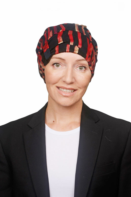A woman wearing a black and red patterned headscarf, a black blazer, and a white top, photographed against a plain white background.