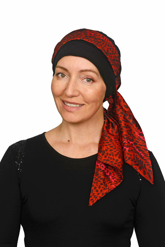 Women wearing a headcovering for cancer that is a scarf and cap seperate in black and a pretty red print