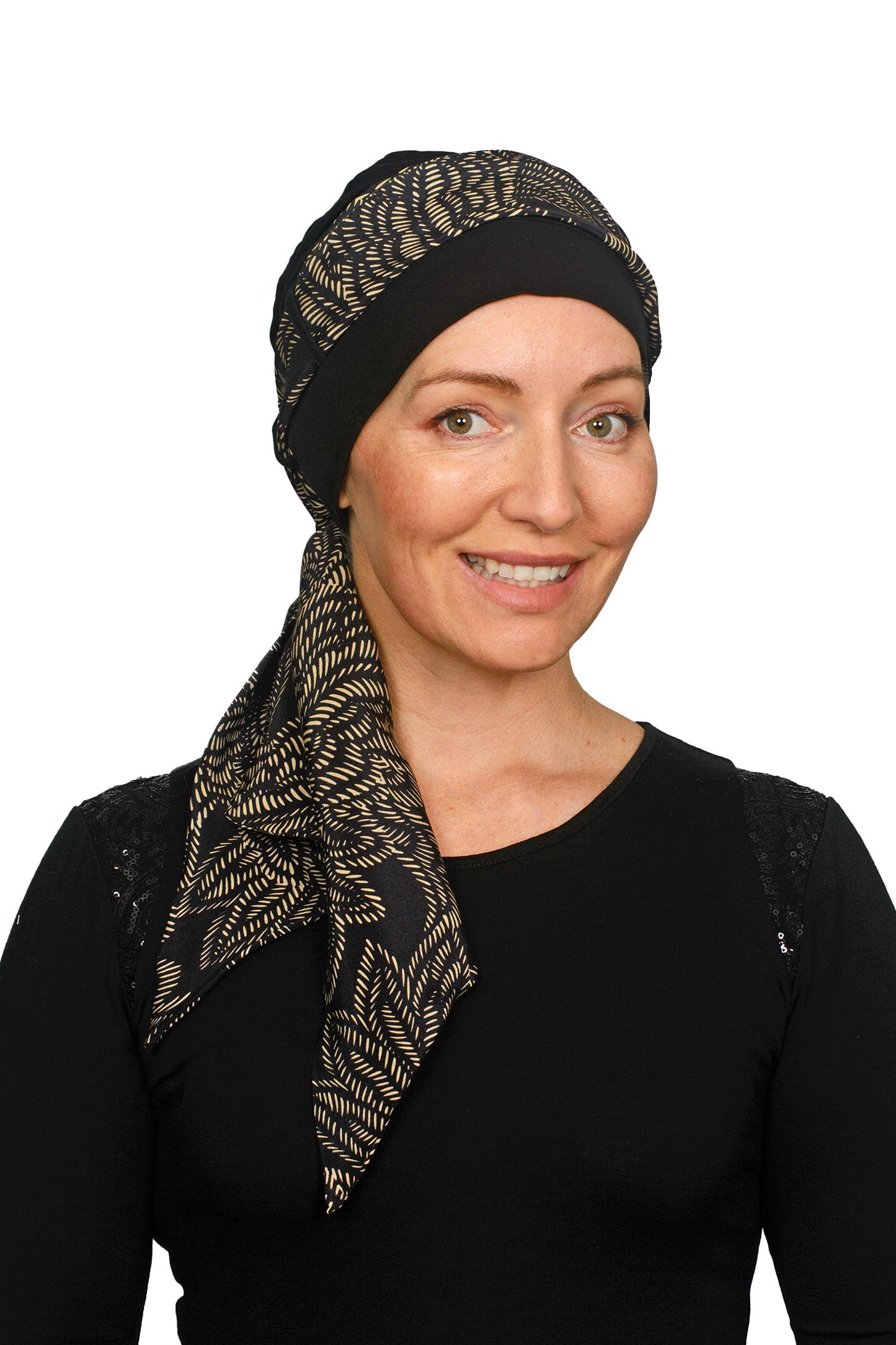 Women wearing a headcovering for cancer that is a scarf and cap seperate in black and a pretty paisley print in sand.