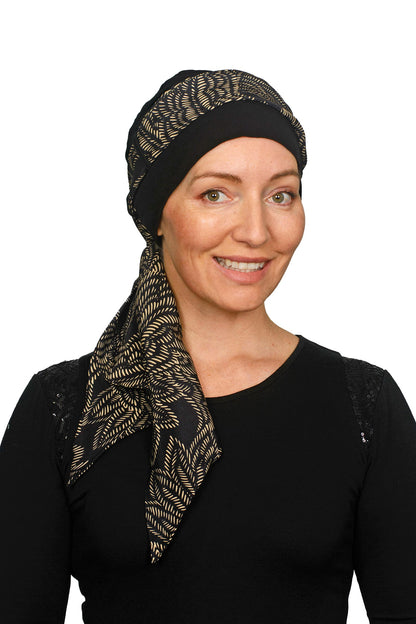 Women wearing a headcovering for cancer that is a scarf and cap seperate in black and a pretty paisley print in sand.