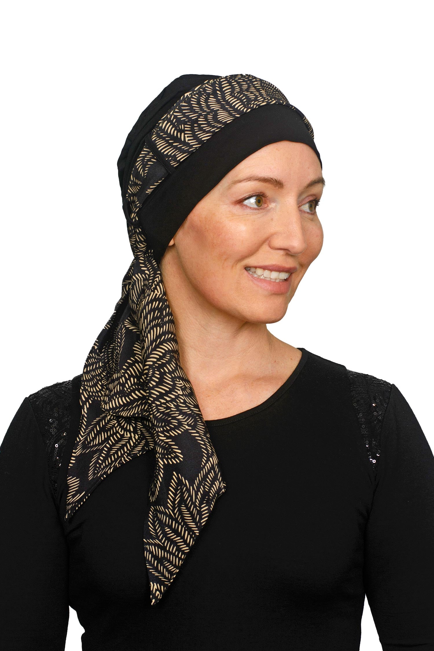 Women wearing a headcovering for cancer that is a scarf and cap seperate in black and a pretty paisley print in sand.