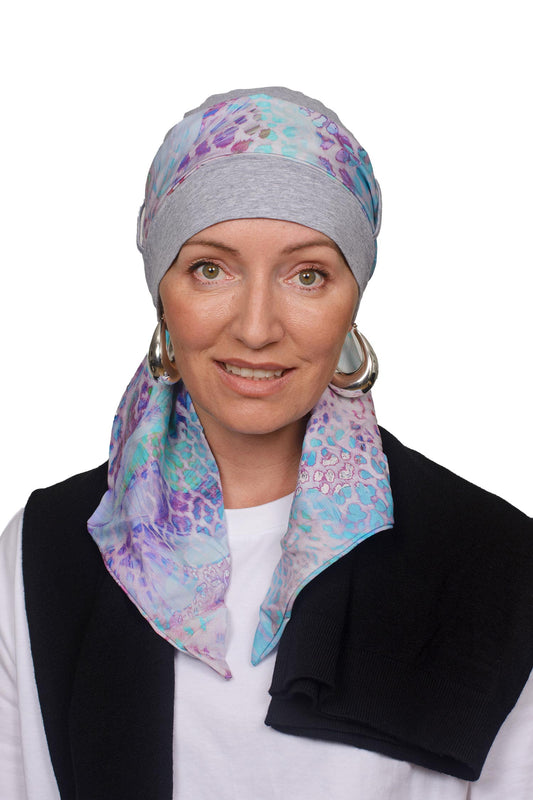 Women wearing a silver marle cap with a light coloured animal print in soft colours scarf through the hat as a headcovering for hair loss