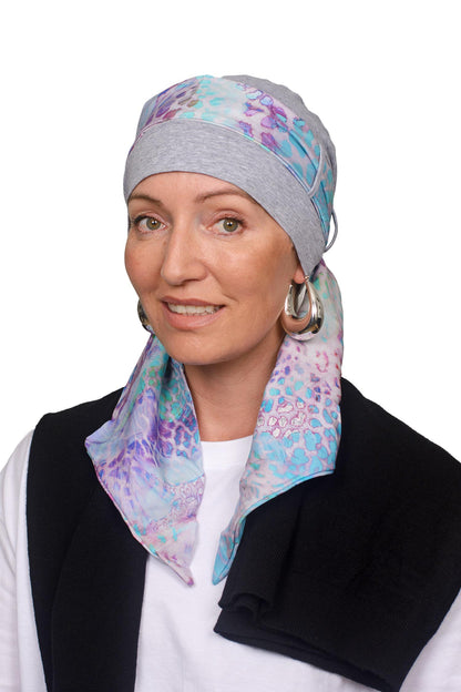 Women wearing a silver marle cap with a light coloured animal print in soft colours scarf through the hat as a headcovering for hair loss