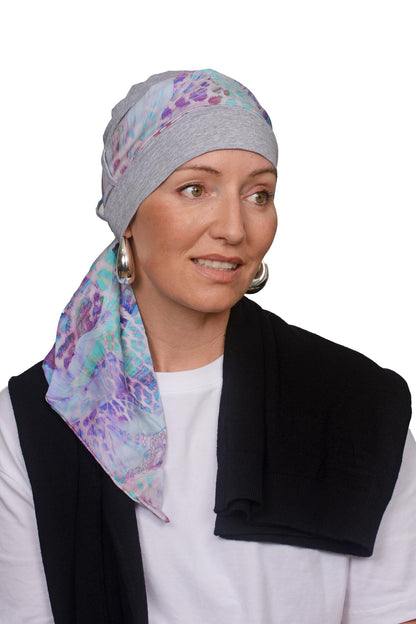 Women wearing a silver marle cap with a light coloured animal print in soft colours scarf through the hat as a headcovering for hair loss