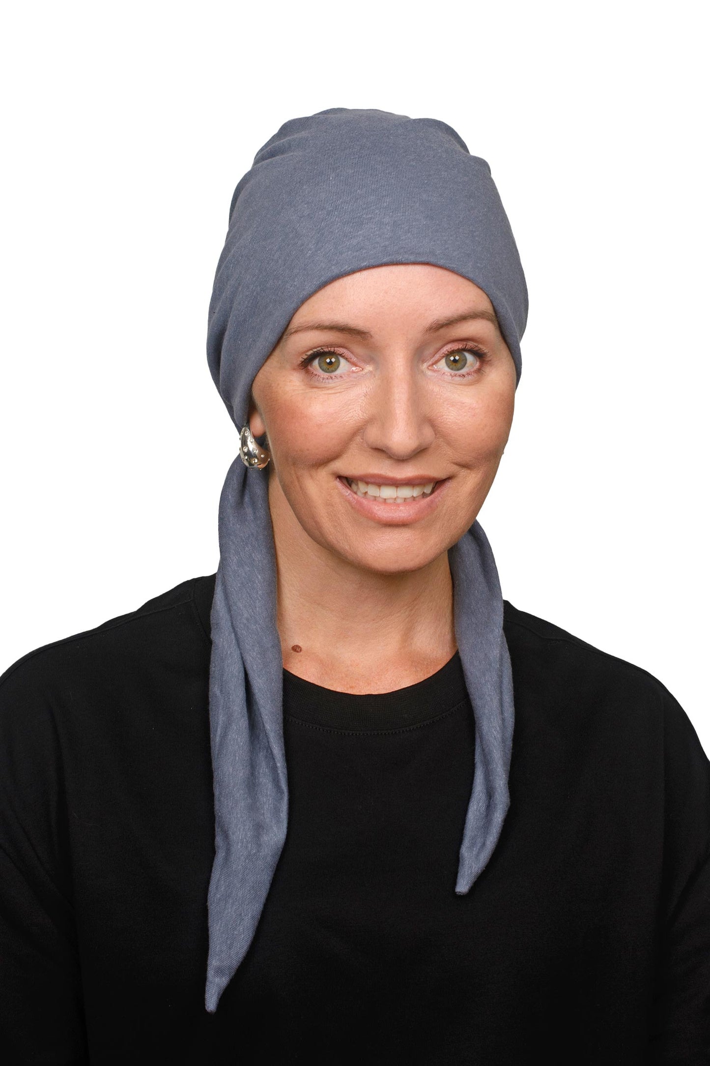 A woman wearing a slate blue fabric cancer head covering or scarf with long hanging tails, styled over her shoulders, set against a plain white background.