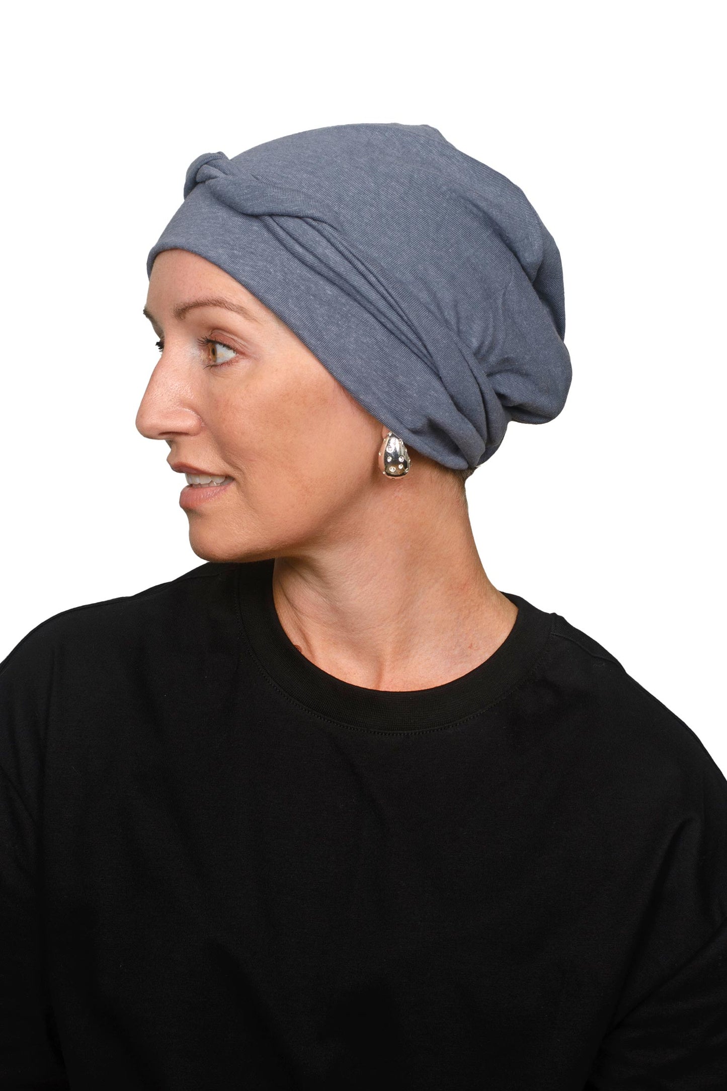 A woman wearing a slate blue fabric cancer head covering or scarf with long hanging tails, styled over her shoulders, set against a plain white background.