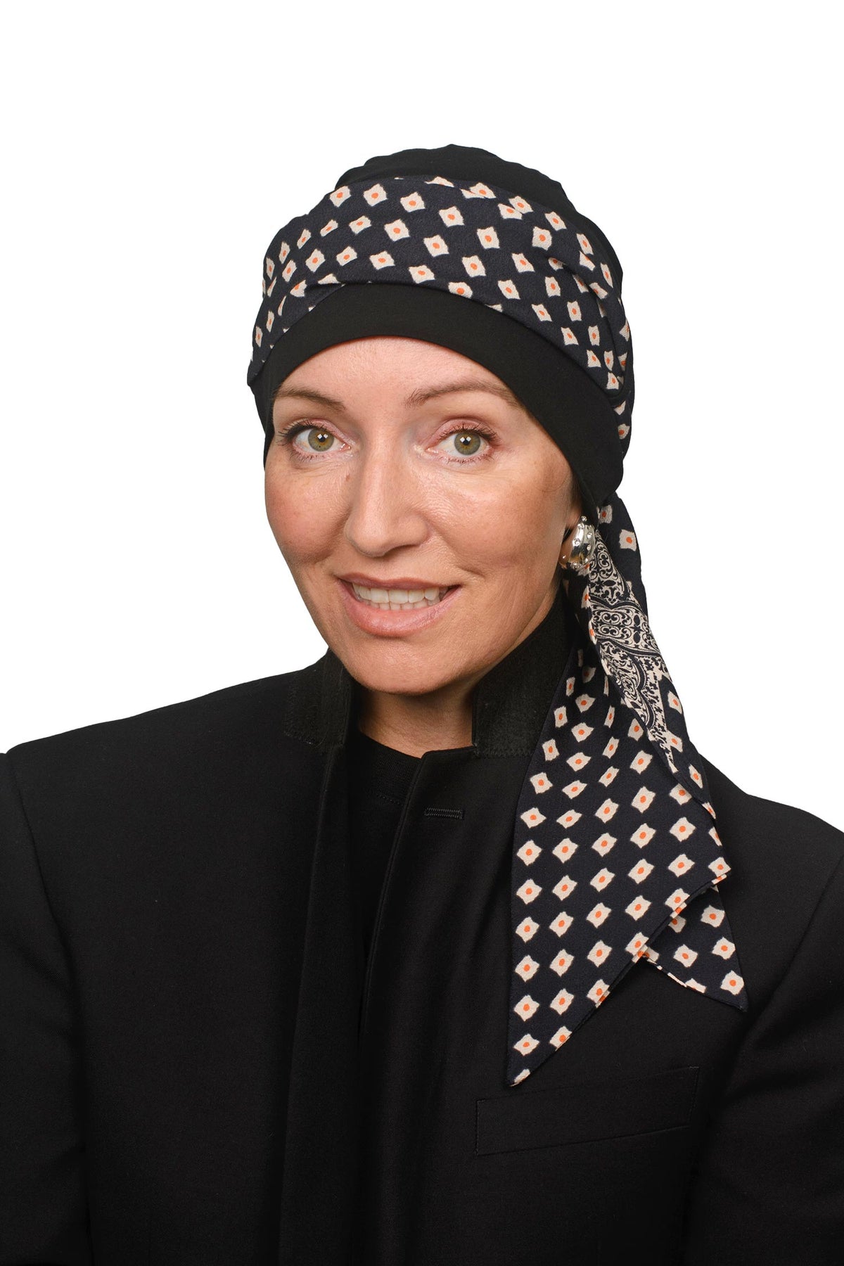 A woman wearing a black headscarf with a beige and white geometric diamond pattern, paired with a black jacket, photographed against a solid white background.