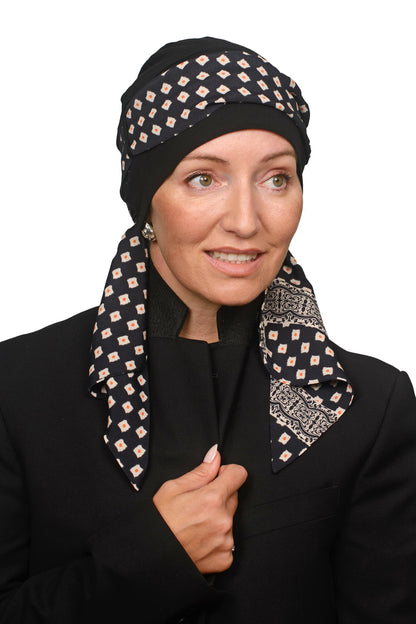 A woman wearing a black headscarf with a beige and white geometric diamond pattern and a matching patterned neck scarf, styled with a black blazer against a plain white background.