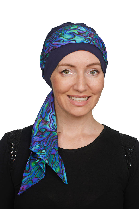 Women wearing a headcovering cancer scarf with cap in an ink and paua design