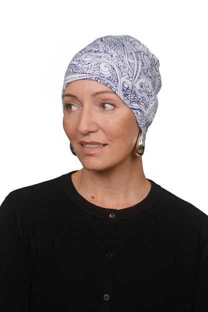 A woman wearing a blue and white paisley patterned fabric head covering, paired with a black top and dangling earrings, photographed against a solid white background.