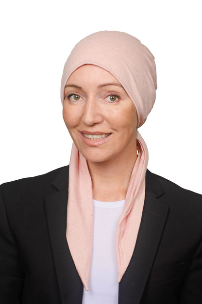 A smiling woman wearing a light pink headscarf and a black blazer over a white top, photographed against a plain white background.