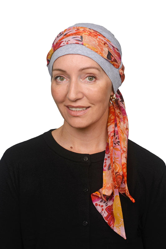 Women wearing a silver cap with a yellow pretty paisley print scarf as a headcovering for cancer