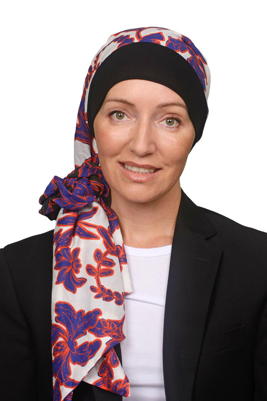 Women wearing a banded scarf hat with a scrunchie in white with blue and orange flowers as a headcovering for hair loss