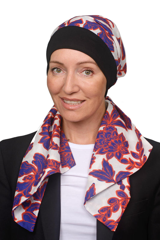 Women wearing a banded scarf hat with a scrunchie in white with blue and orange flowers as a headcovering for hair loss